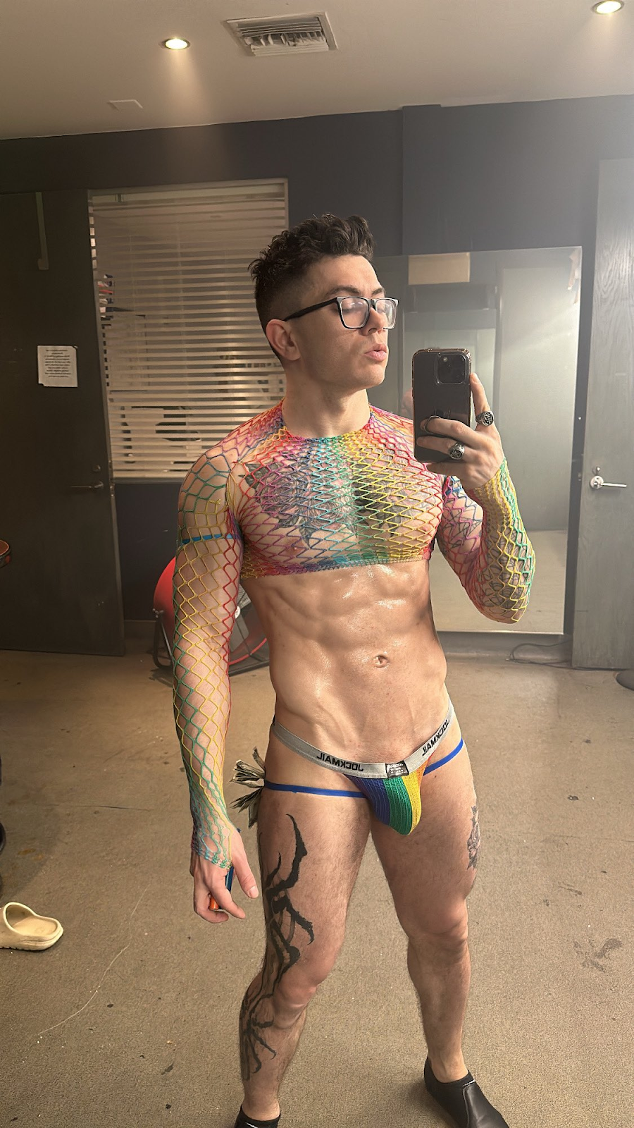 Clark Davis wearing rainbow jockmail and rainbow mesh shirt taking mirror selfie covered in sweat at the strip club