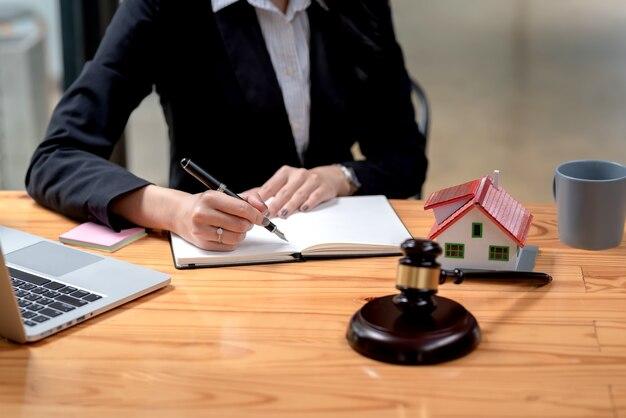 Photo close-up of a woman lawyer holding a pen and taking notes on a sample house mallet placed at the office desk.