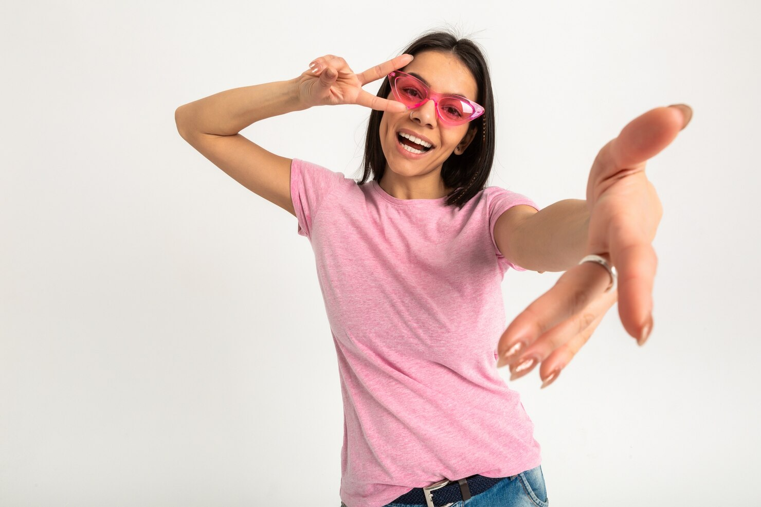 A girl in a pink t-shirt and sunglasses makes a victory sign.
