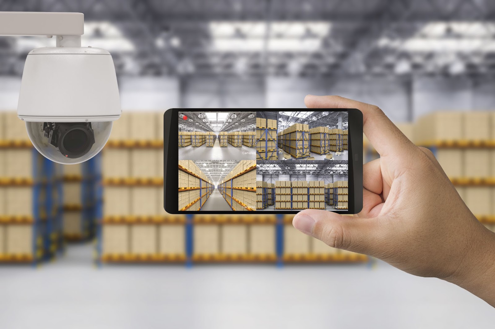 Hand holding a smartphone with a live security camera feed of warehouse shelves, highlighting surveillance technology.
