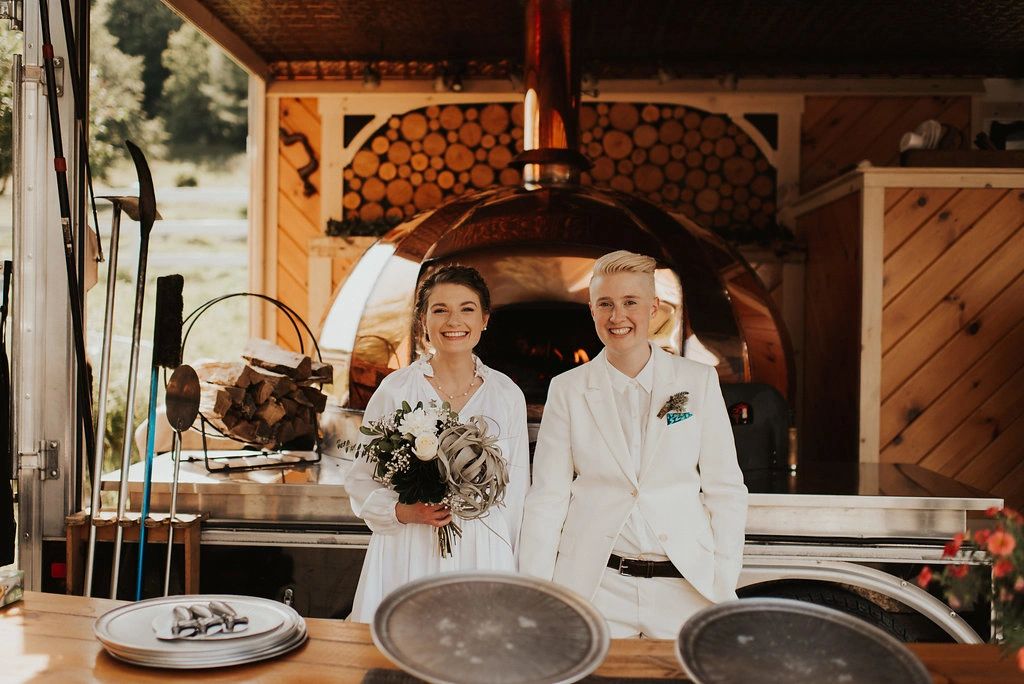 Couple standing in front of wood-fired pizza oven