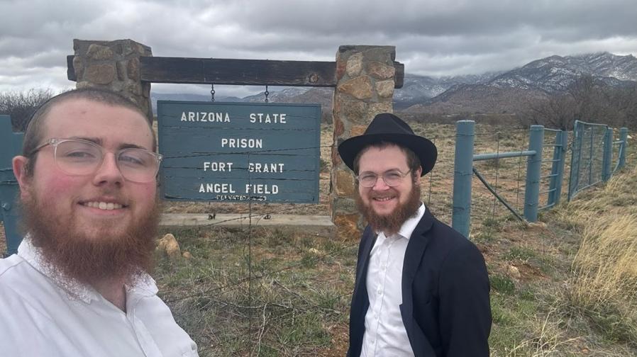 Two men standing in front of a sign

Description automatically generated