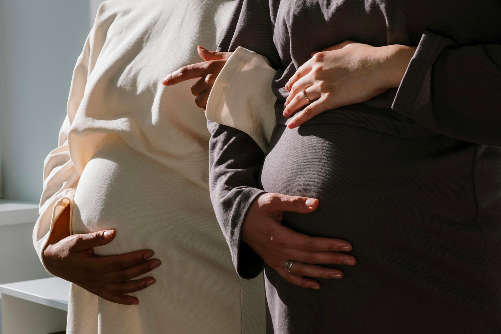 Two pregnant women holding their stomachs, one in black and one in white