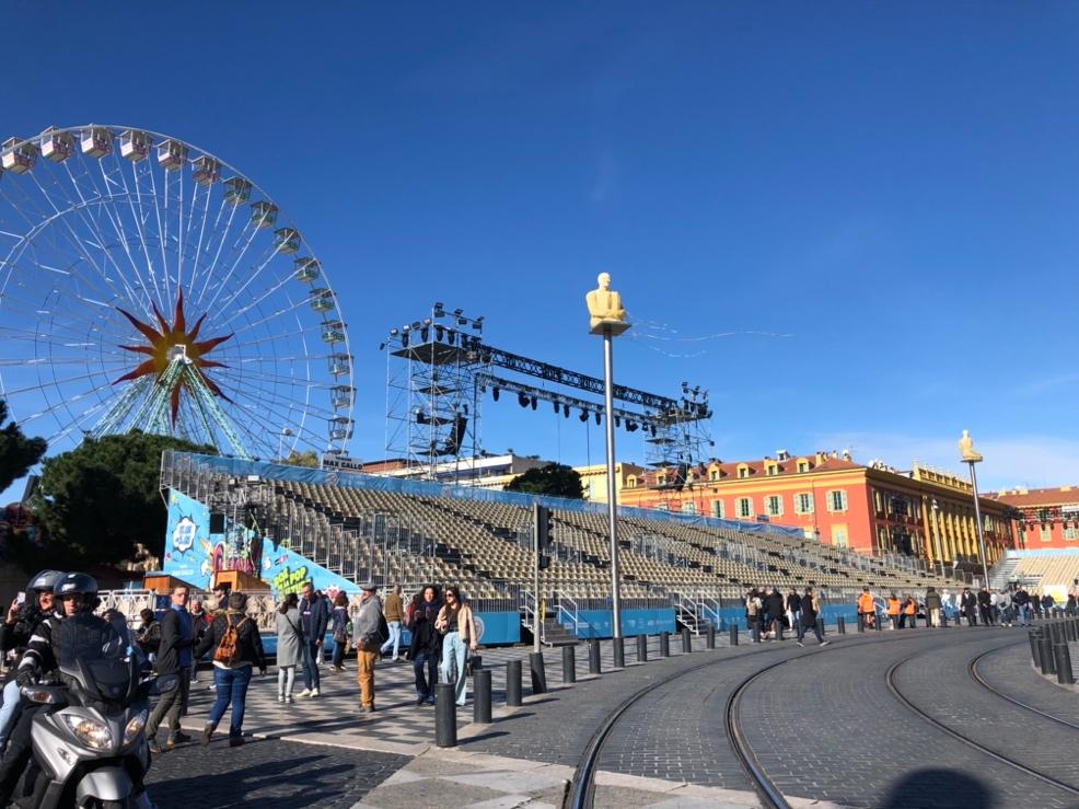 A crowd of people walking around a ferris wheel

Description automatically generated