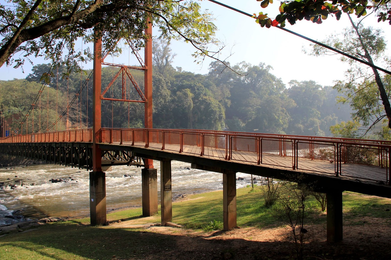 Ponte que passa sobre o Rio Piracicaba, SP. A grande estrutura de metal vermelha está cercada por trechos de mata nativa