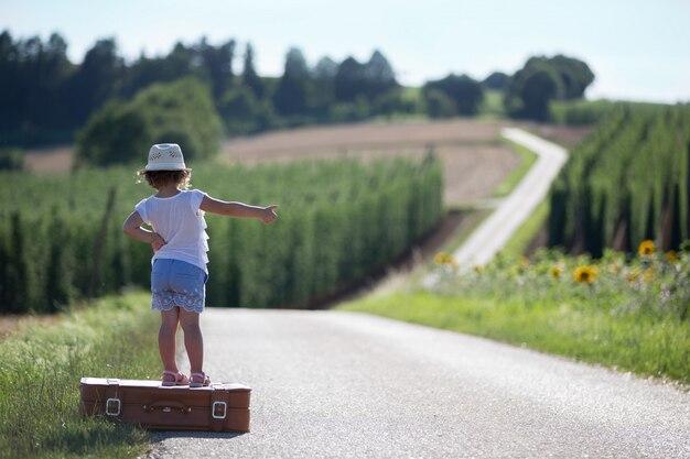 Foto una niña con una maleta en una carretera entre dos campos