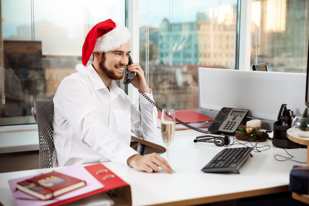 A businessman calling on the landline while wearing a Santa hat.