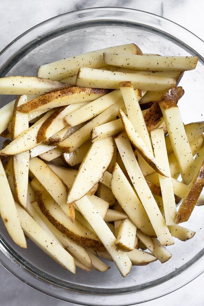 Toma aérea de patatas crudas cortadas en patatas fritas en un bol grande.