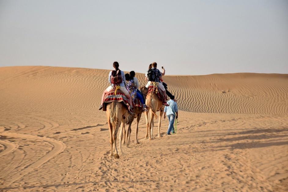 A group of people riding camels in the desert

Description automatically generated