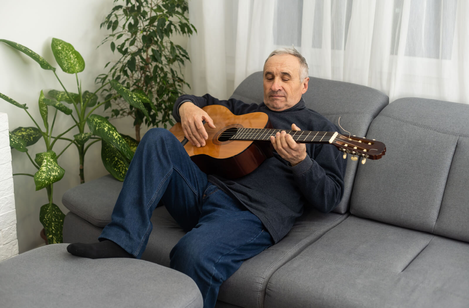 An older adult man playing a guitar while sitting on a couch.