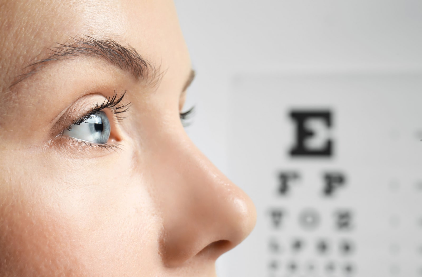 A close up image of a woman looking away from the camera, and she is standing in front of a Snellen eye chart