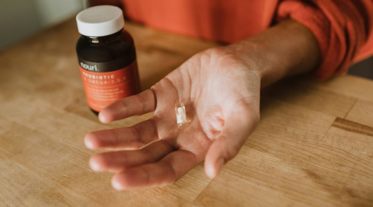 Capsule de probiotiques dans une main avec le contenant en fond