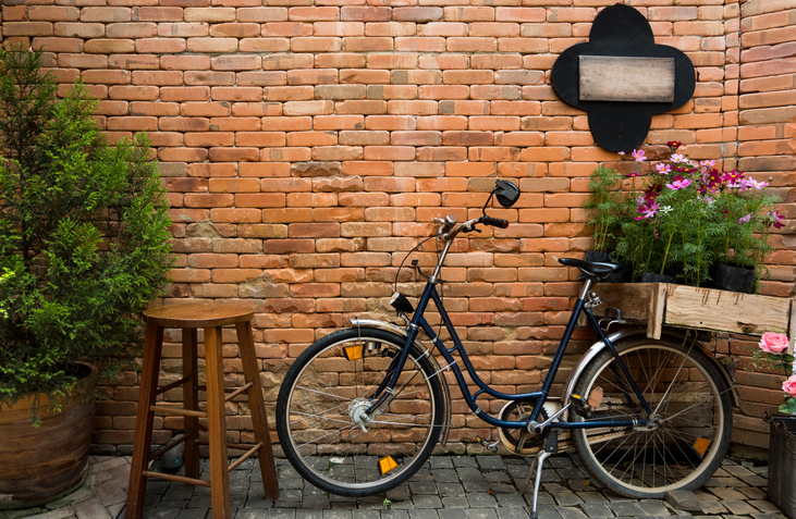 A bicycle leaning against a brick wall beside a wooden stool. 