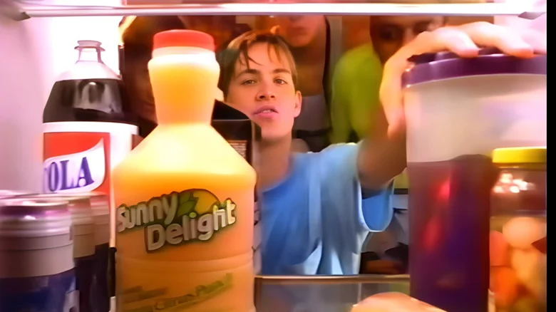 A young man gazes at a bottle of Sunny Delight in the fridge.
