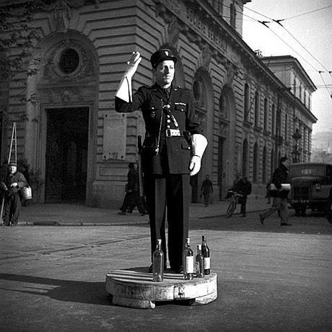 A person in a uniform standing on a platform with bottles on it

Description automatically generated