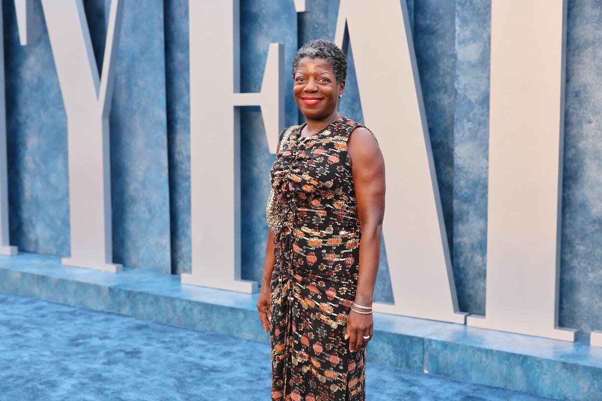 A smiling woman in a dress standing on a blue carpet.