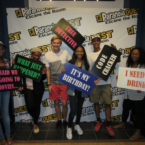 A group of friends holding banners after a escape room game birthday celebration. 