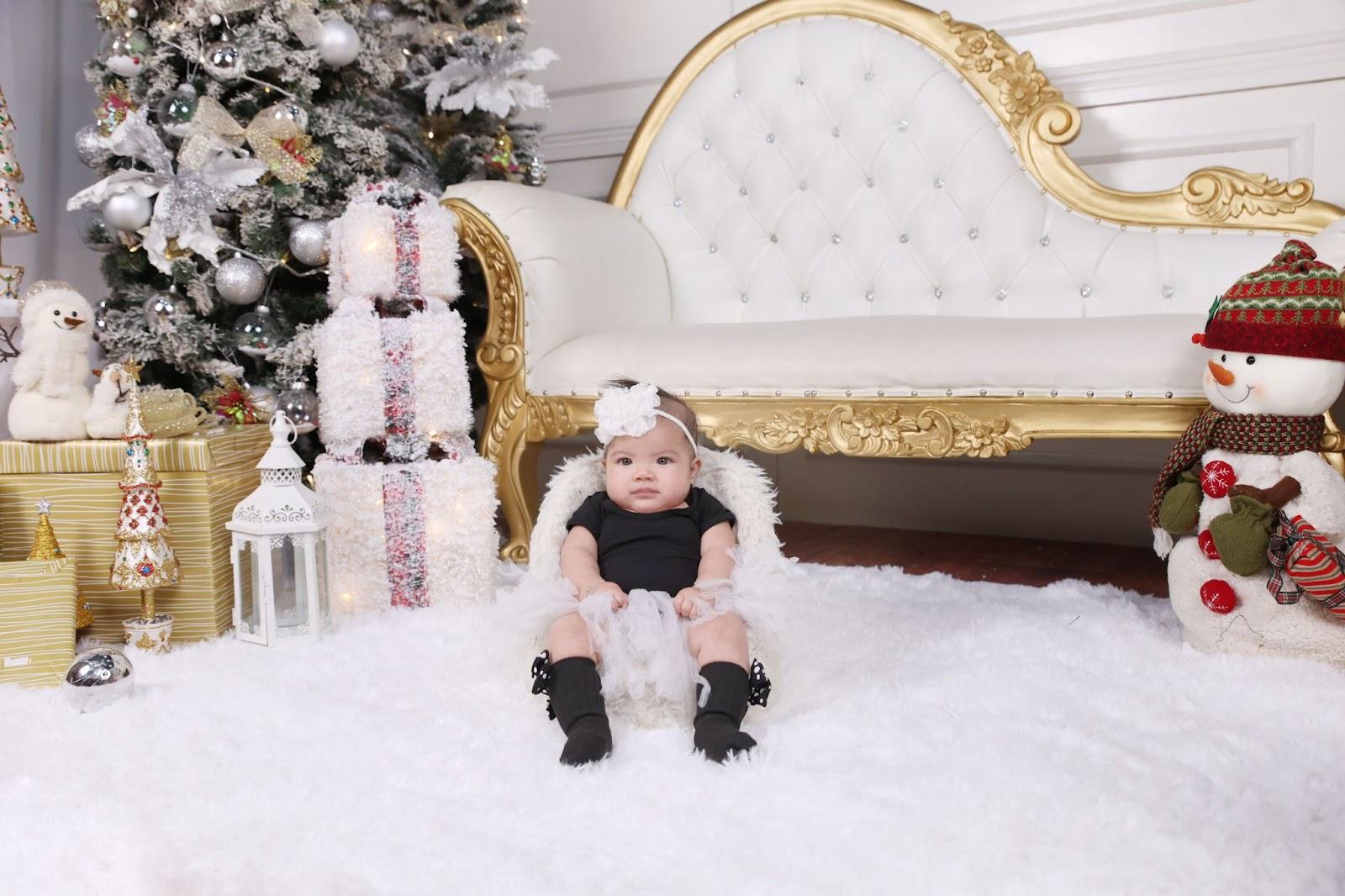 newborn christmas photo idea: baby dressed up in winter outfit while seated on a sofa bed amidst a winter wonderland decor
