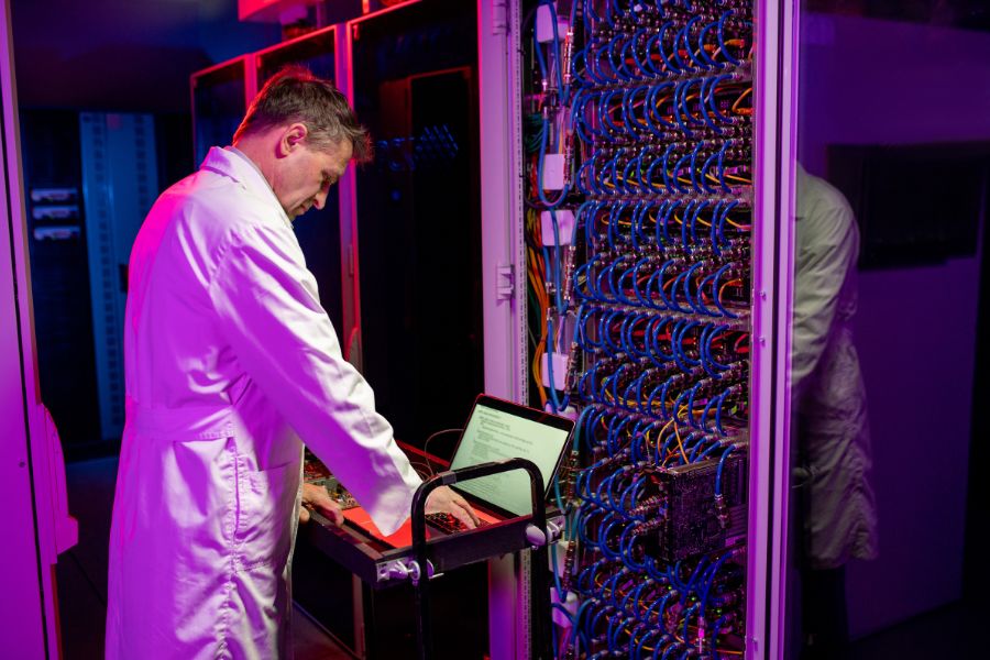 Person in a lab coat working on a computer in a server room.