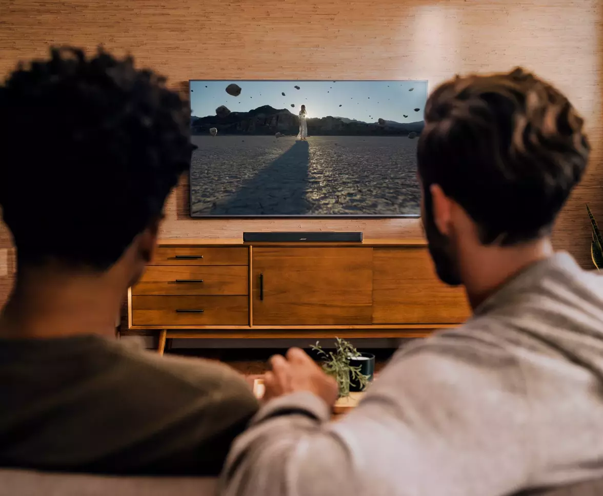 Two men enjoying a movie on a TV in a living room, enhanced by the immersive sound of a Bose TV speaker.