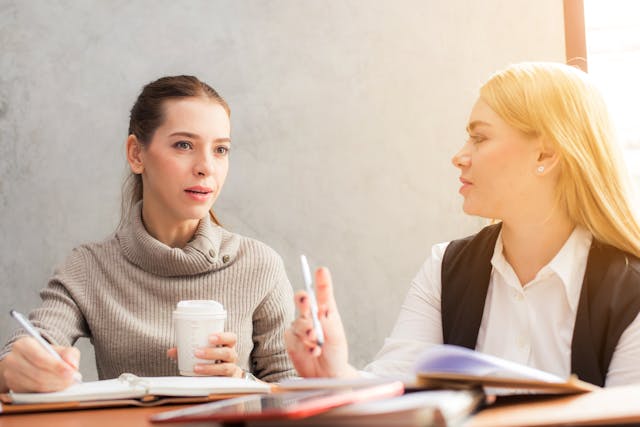 Two women talking with a pen and notebook