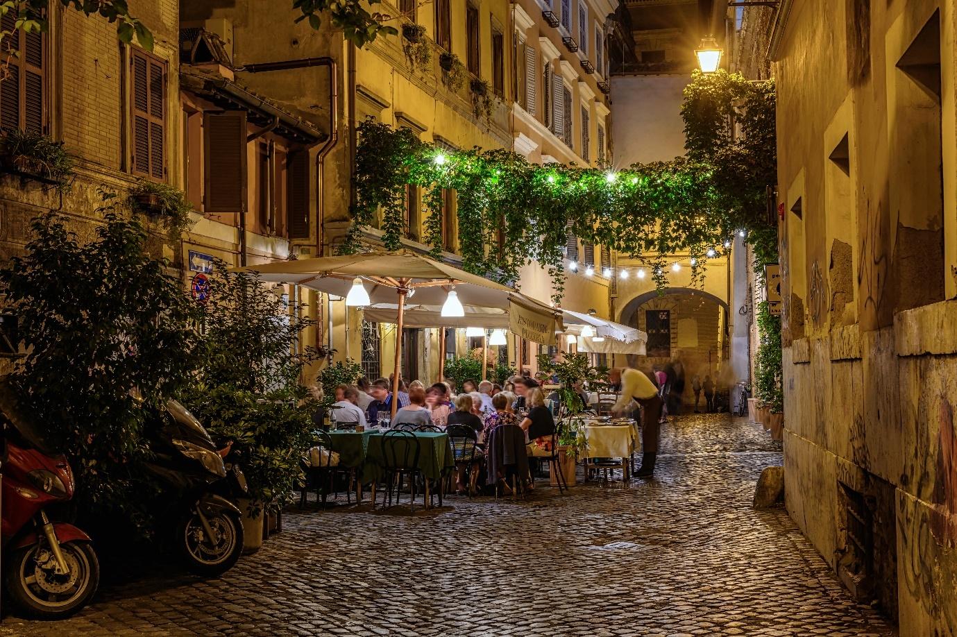 A group of people sitting at tables in a courtyard

Description automatically generated