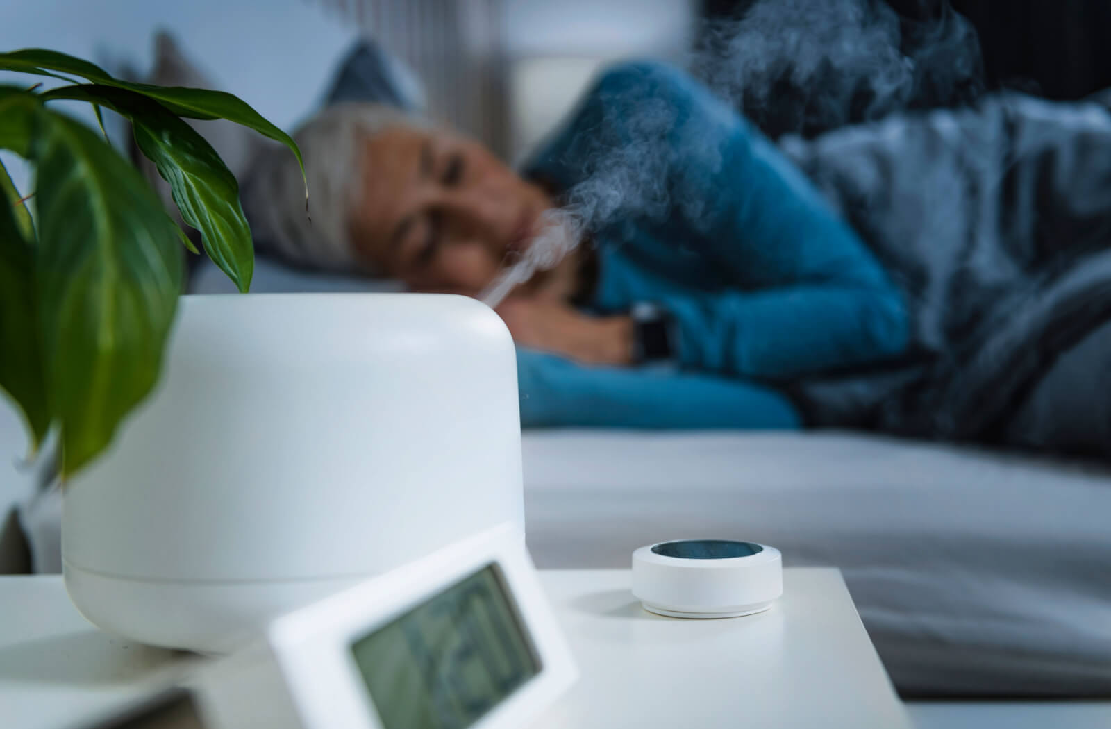 A humidifier on a nightstand beside a sleeping woman.
