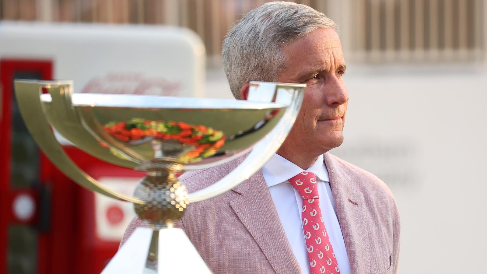 jay monahan stands in a pink suit next to fedex cup trophy
