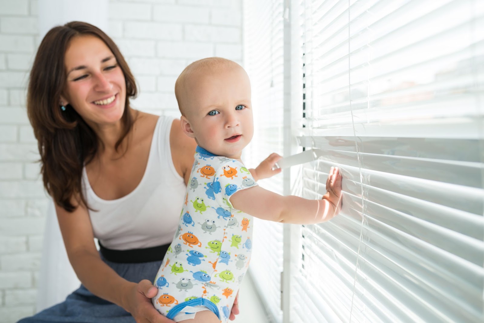 Mom looking at kid holding the child-safe window blinds looking at the camera