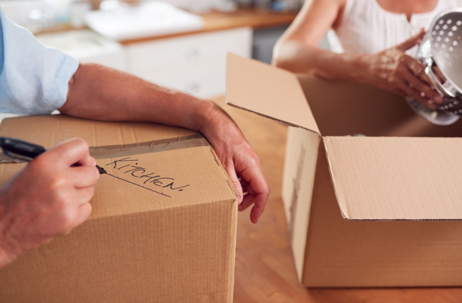 A senior couple packing boxes with kitchen items in them