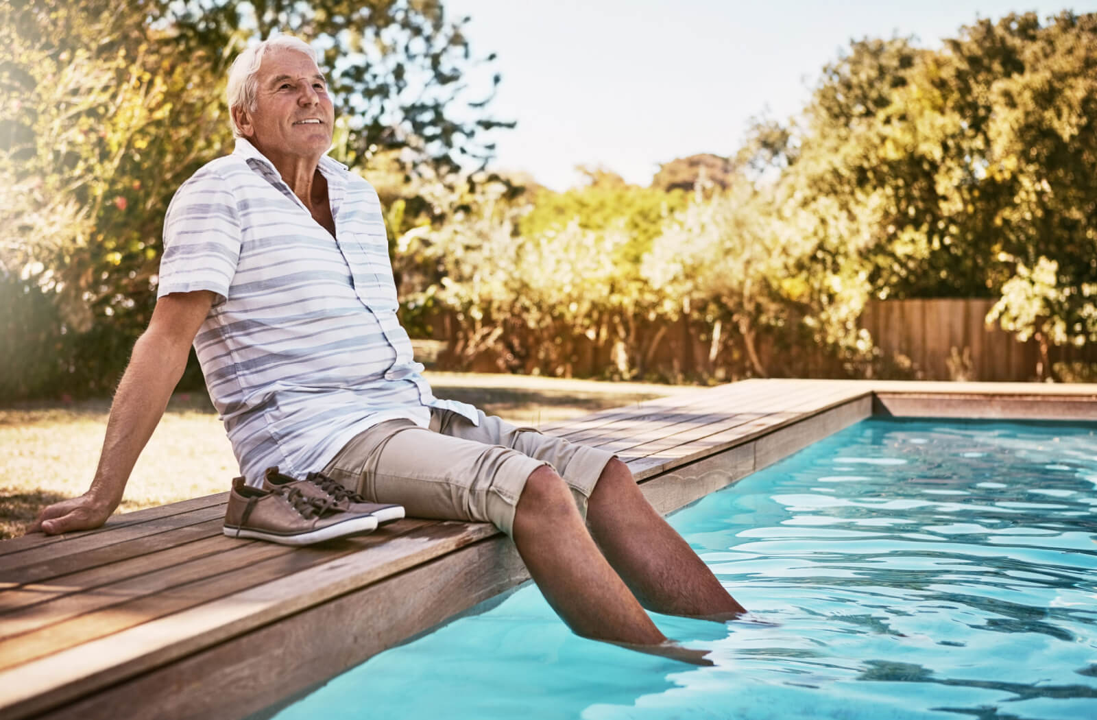 An older adult man resting by the poolside and dipping his feet in the pool.
