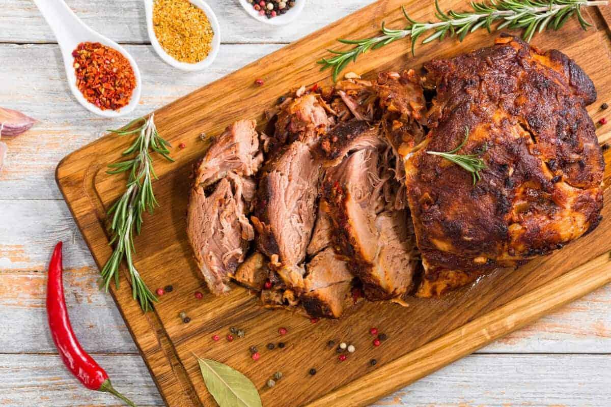 Umăr de porc la grătar, feliat pe o masă de tăiat, cu rozmarin și chilis