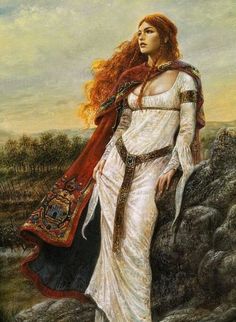 Goddess Caer is wearing a red ancient Celtic cloak while standing in front of a stone wall next to a field.