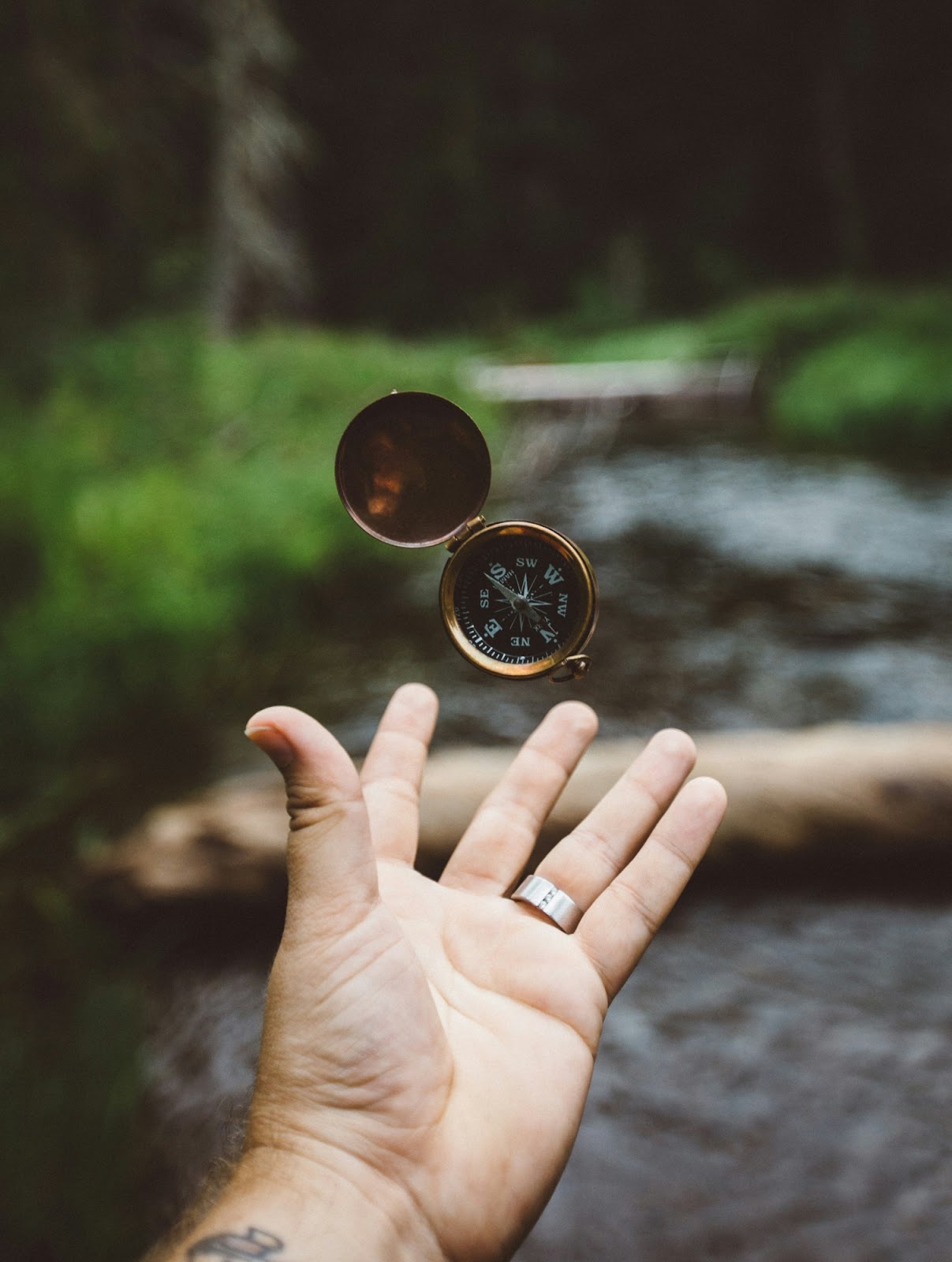 A person’s hand catching a compass in front of an out-of-focus riverbed.