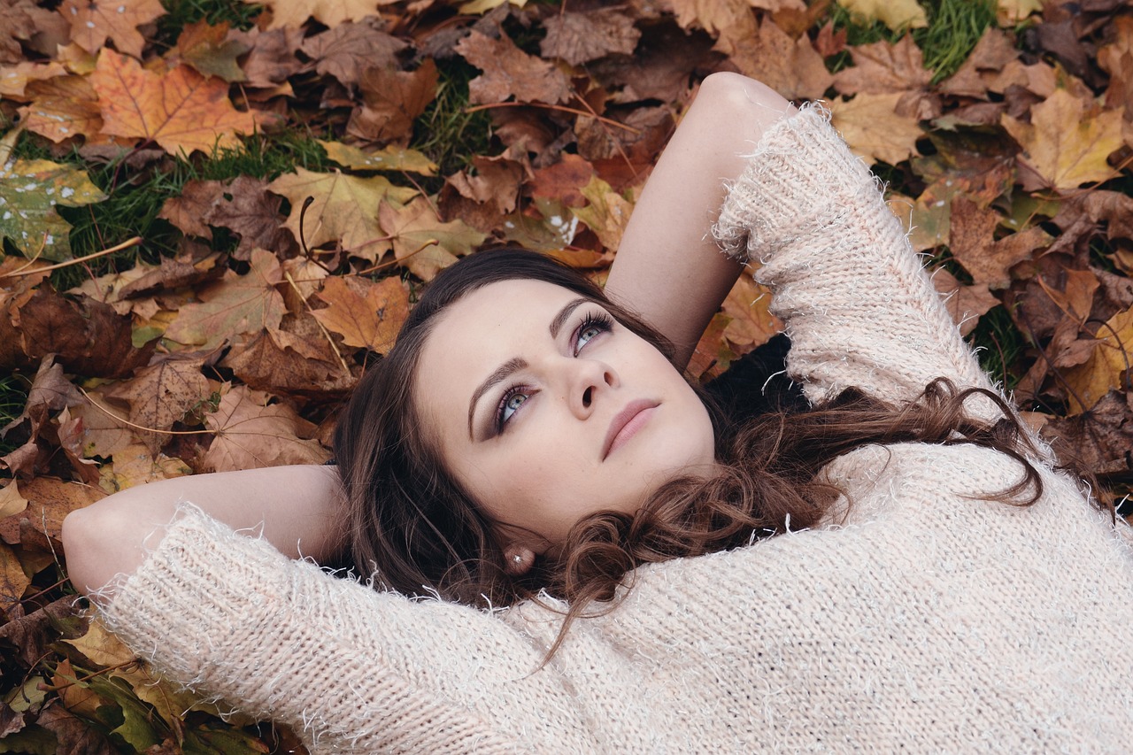 A girl looking up at the sky while lying in a bed of leaves.
