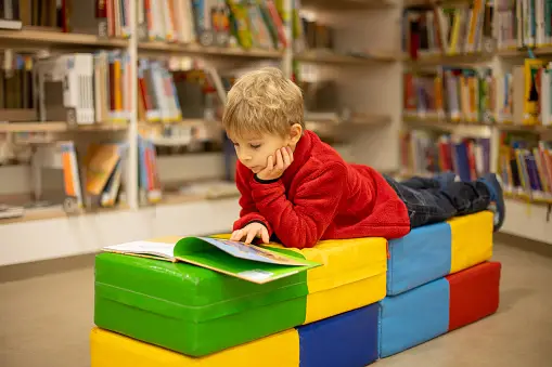 Little Boy in Red Shirt Laying on Soft Blocks Reading a Book