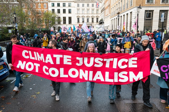 Rebels march with a banner that says 'Climate Justice Not Colonialism'