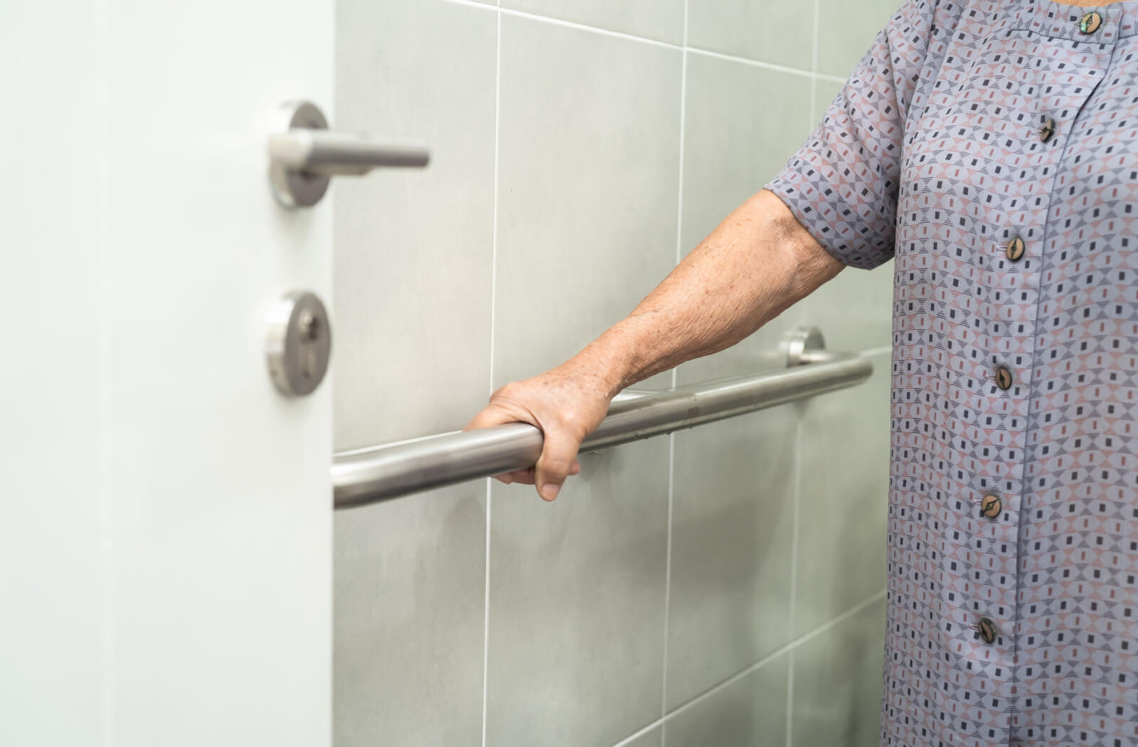 An older adult holding on to a grab bar in her bathroom.