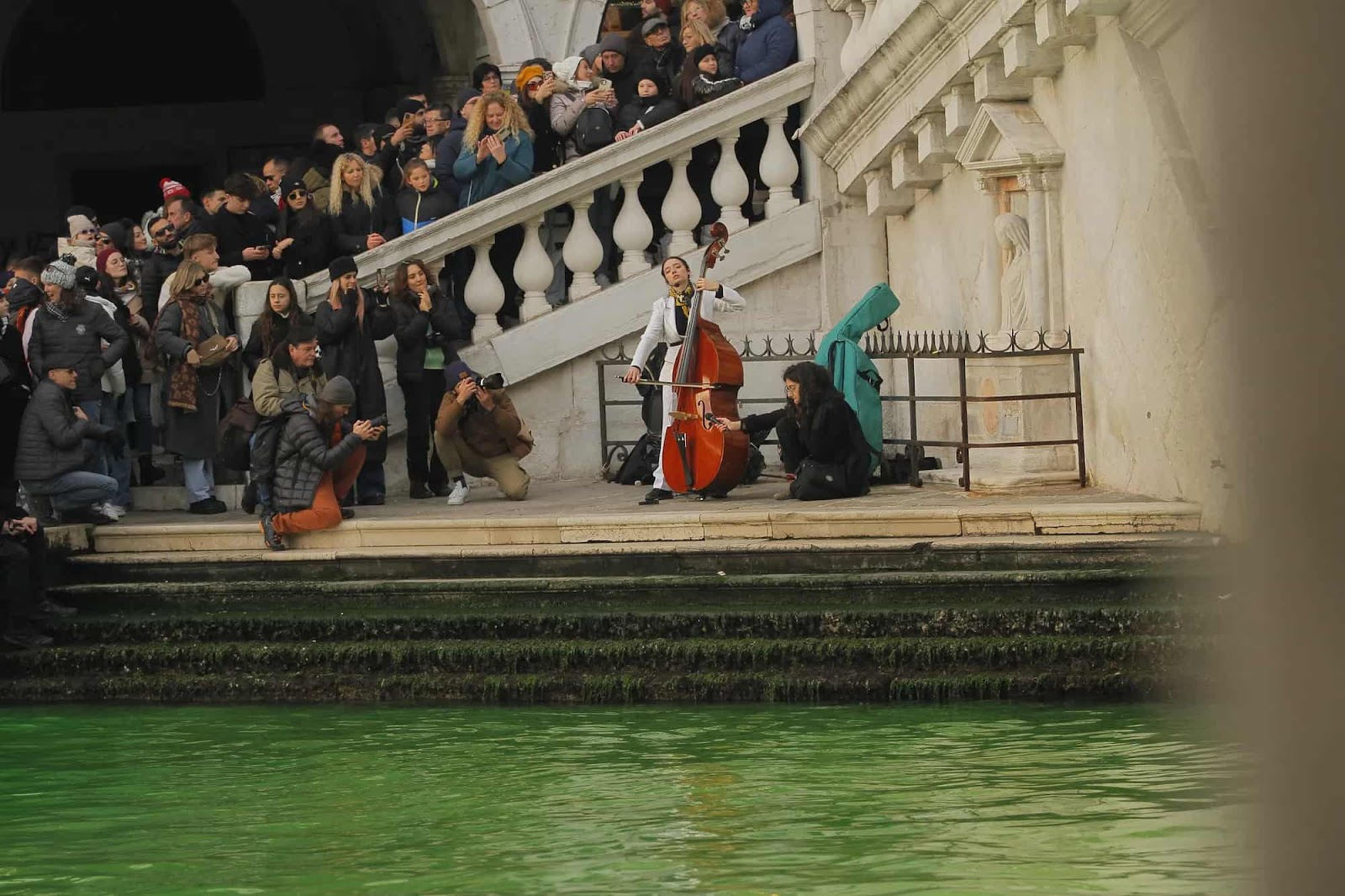 A rebel plays her double bass beside a Venetina canal bridge as a crowd listens
