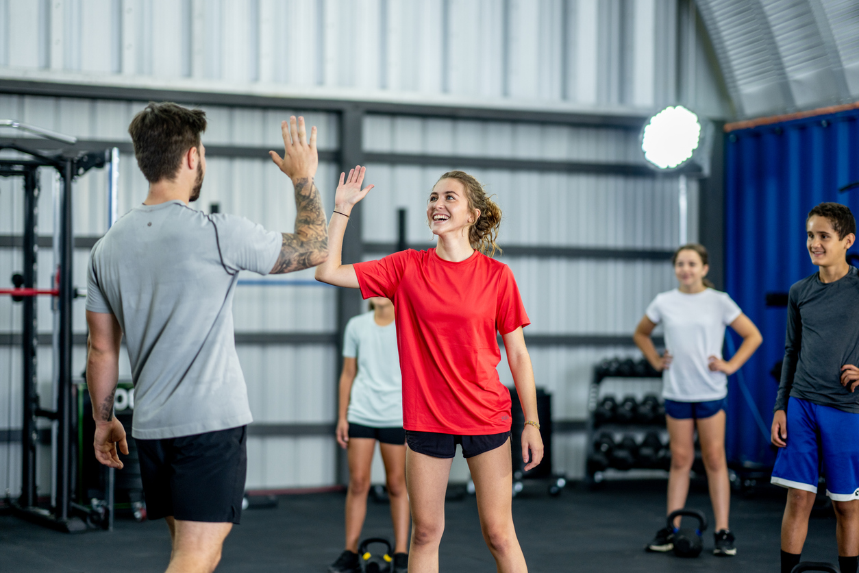 A fitness instructor high-fives a young woman as they celebrate a successful workout and achieving goals.