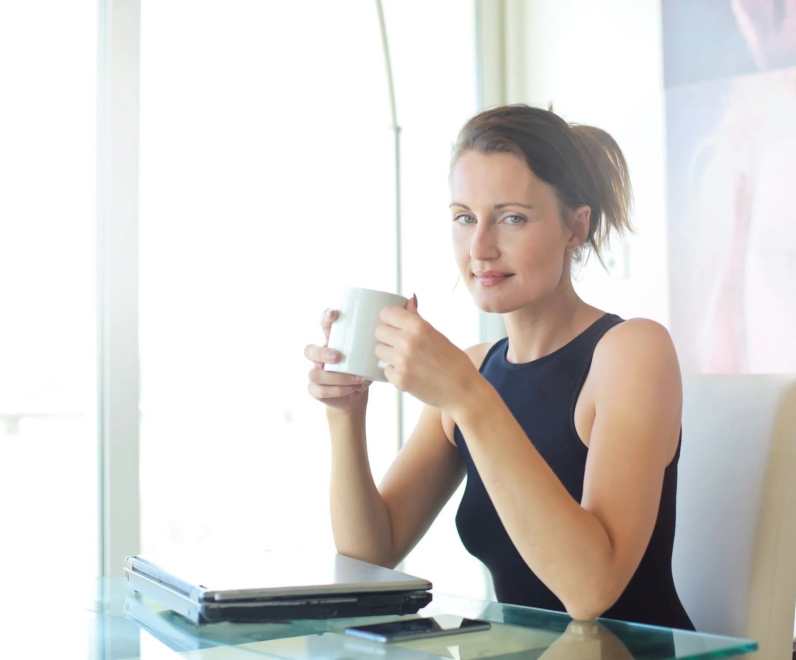 business woman holding a mug of coffee near a laptop and smartphone