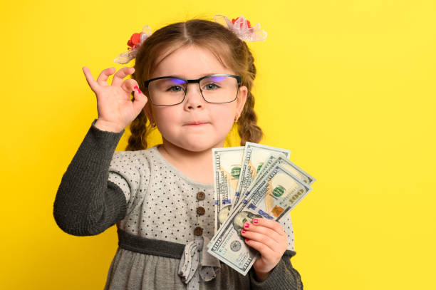 money-and-children-on-the-background-a-rich-girl-with-glasses-holding-picture-id1322150647?k=20&m=1322150647&s=612x612&w=0&h=I1rZeDQr922RjP8sZIyW0foQErt65eqx3C81kRX3qQs=