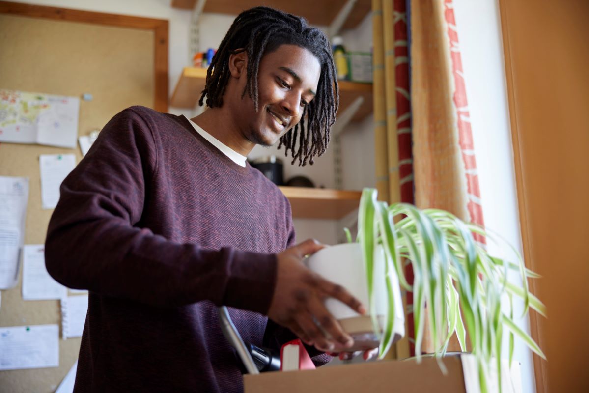 College student moving into an on-campus dorm room and unpacking a plant.