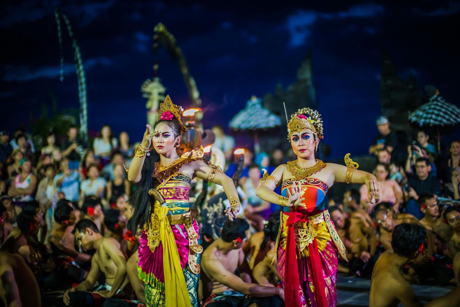 two indonesian women wearing traditional bali outfit dancing in the night among the crowds