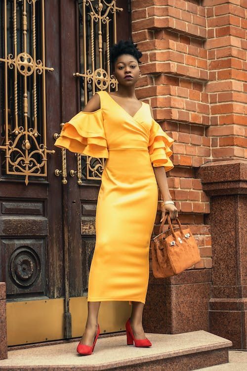 A classy girl posing in front of a building wearing a yellow dress