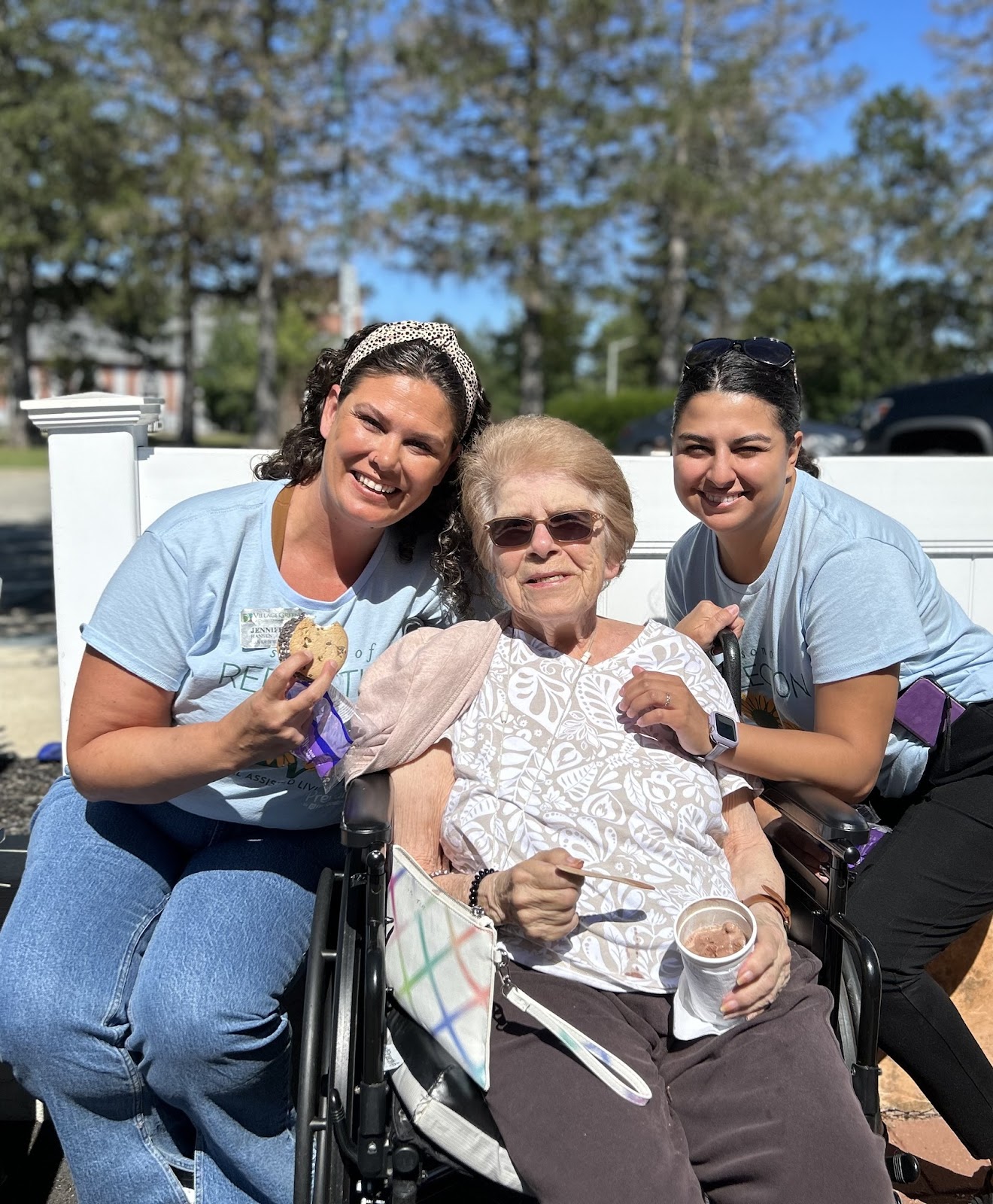 A woman smiling in a wheelchair next to her caregivers who are smiling