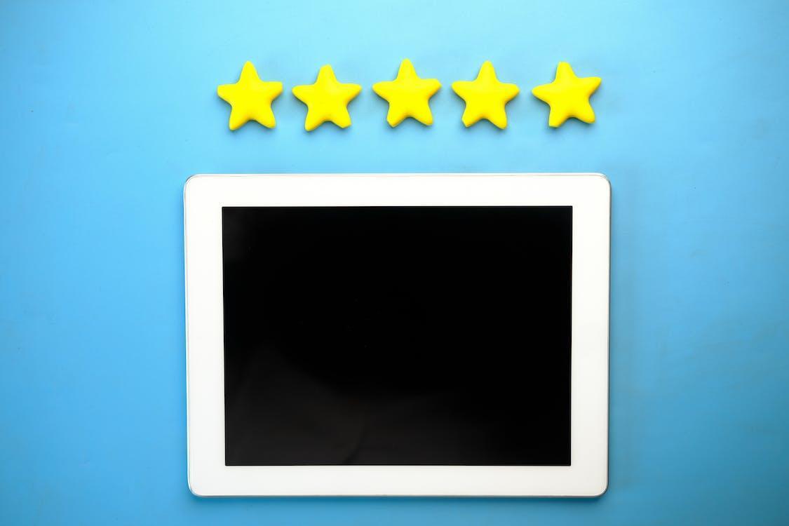Four bright yellow stars above a blank tablet screen on a blue background, representing high online review ratings for a small business leveraging AI website technology.