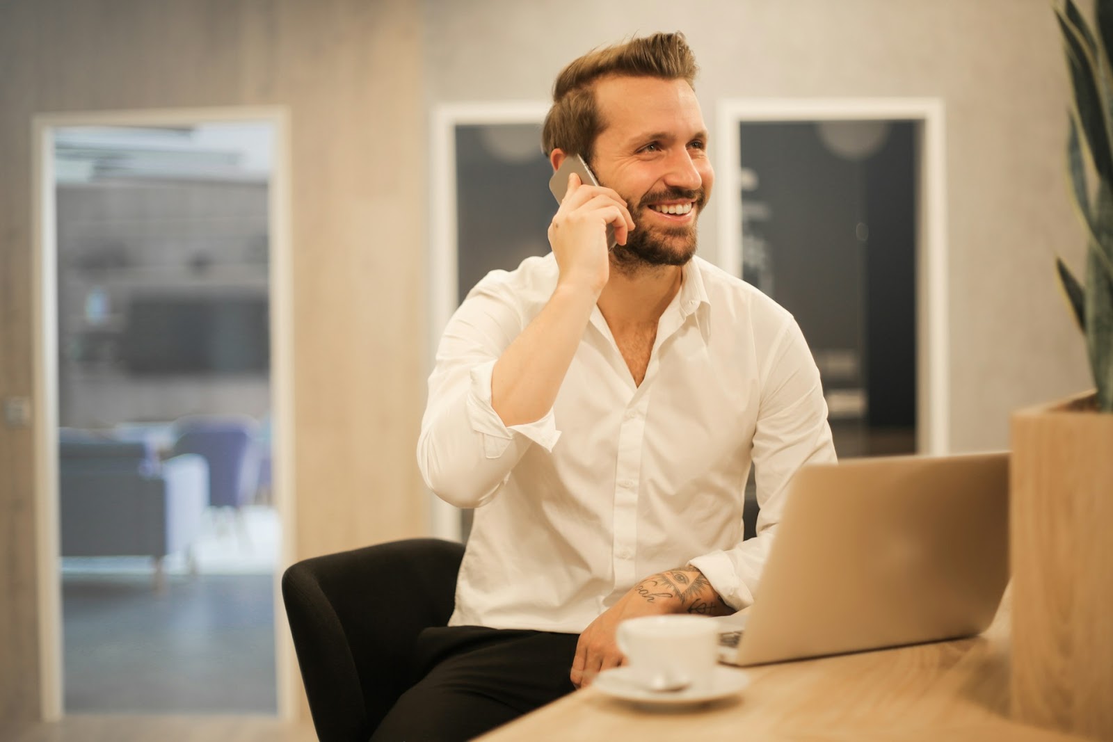 A person at a desk with a laptop, coffee, and talking on the phone.