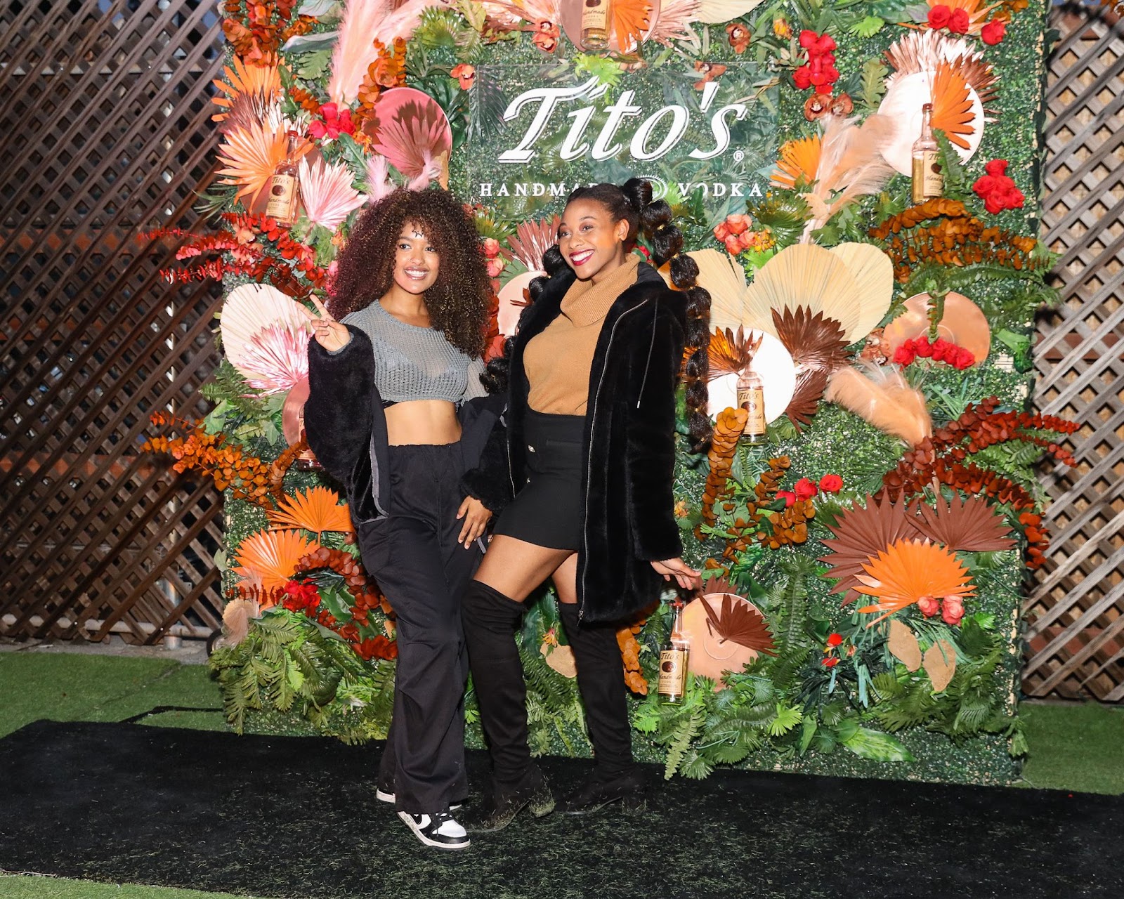 Two highly fashionable women of color taking a photo in front of Tito's Vodka photo booth