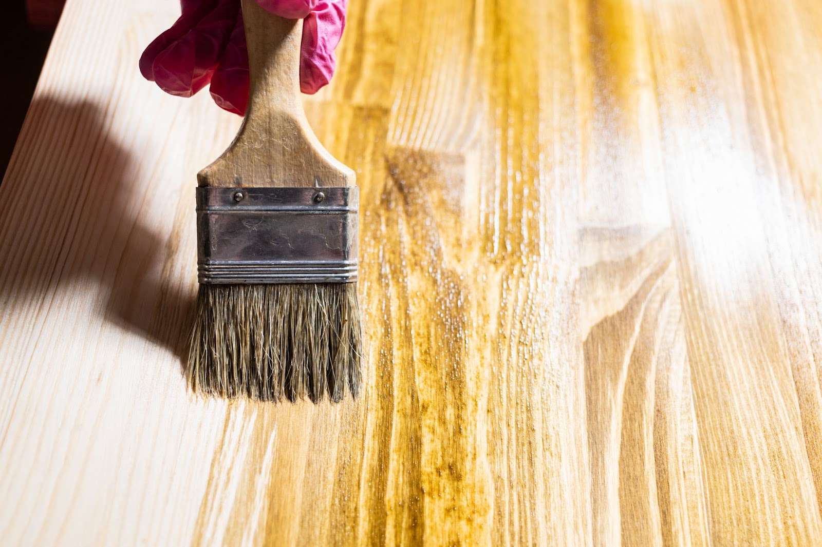 A worker uses a paintbrush to paint the wooden board with wooden stain. 